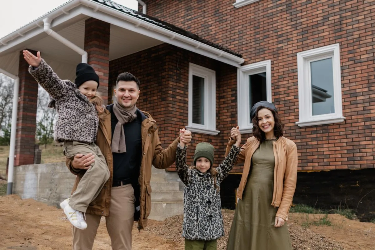 Smiling family of four holding hands in front of their new brick home