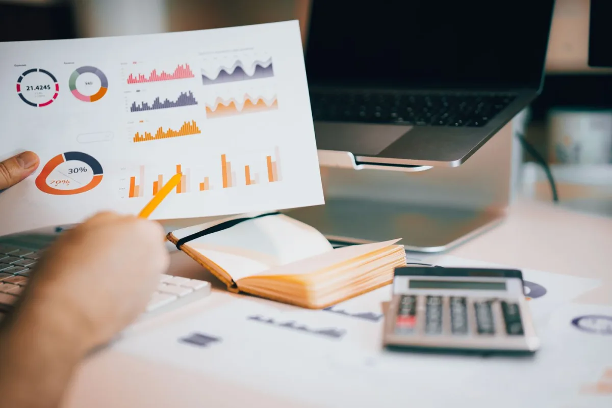 Printed market charts, a calculator and a notebook spread across a desk